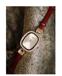 Macro shot of gold oval watch dial with rhinestones and red leather strap on wood