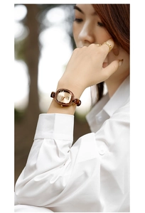 Close-up of a women's vintage oval watch with gold case and brown leather strap on wrist