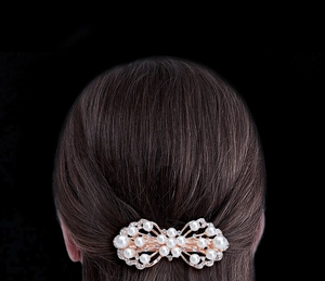 Detail of rose gold bow hair clip with pearls and rhinestones worn on brown hair