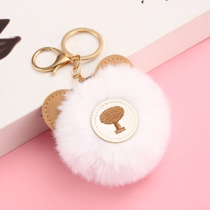 Detail of white faux rabbit fur pom pom keychain with brown bear ears on pink background