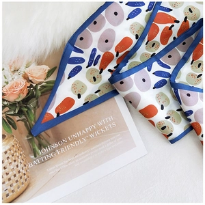 Detail of elegant silk scarf with orange fruit patterns and blue borders on a lifestyle backdrop