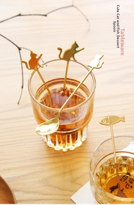 Golden cartoon cat and fish dessert spoons hanging on a glass cup in tea time setting
