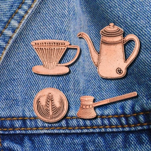 Detailed view of coffee themed bronze pins pinned on blue denim jacket fabric