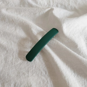 Macro view of long rectangular matte dark green hair clip on white linen fabric
