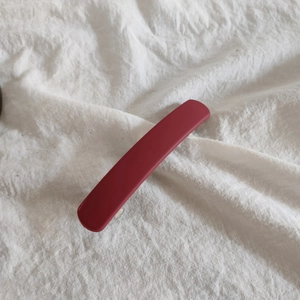 Close-up of a deep red matte acrylic hair clip on white textured fabric background