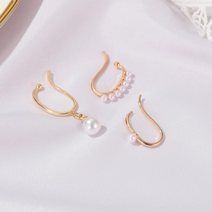Detailed shot of three gold-plated pearl ear cuffs set on elegant white silk fabric