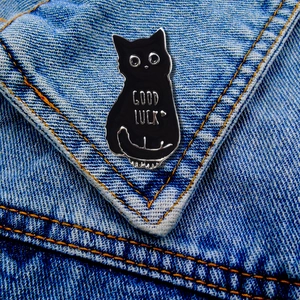 Cute black enamel cat brooch with Good Luck text pinned on blue denim jacket