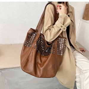 Detail view of large brown studded tote bag with leather texture and silver rivets