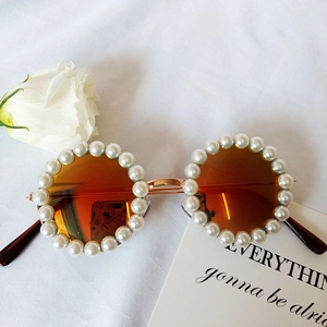 Flat lay of round pearl sunglasses with orange lenses and white rose on fabric