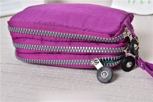 Detailed view of purple triple-zipper coin purse with large round pulls and wrist strap