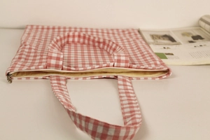 Detail view of pink gingham canvas bag with secure white zipper closure and yellow lining