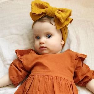 Detail of mustard yellow waffle texture bow headband and rust orange baby dress
