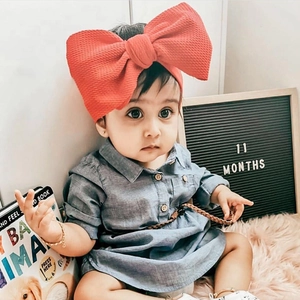 Close-up of a red textured oversized bow headband worn by a baby girl in a blue dress