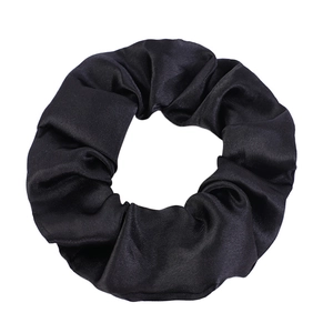 Detailed view of black satin scrunchie showing glossy fabric texture and elastic pleats