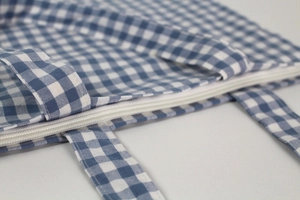 Detailed close-up of the white zipper closure and stitching on a blue checkered canvas bag