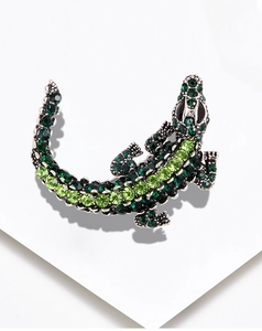Close-up of a sparkling green rhinestone crocodile brooch on a white textured surface
