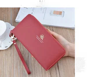 Detail of red litchi texture long wallet with gold clover logo and wristlet strap