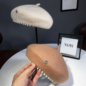 Close-up of wool beret hats with pearl trim and metal M letter detail in cream and camel