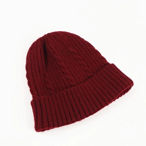Detail shot of the chunky cable knit texture and ribbed cuff on a wine red beanie hat