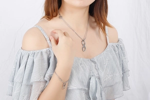 Silver infinity and heart necklace set displayed on a model against white fabric