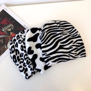 Flat lay of knit beanies in leopard, zebra, and cow animal prints for winter fashion