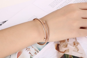 Close-up of rose gold minimalist twisted cable open bangle on model wrist with magazine