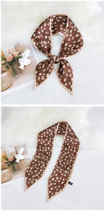 Detail showing the brown floral silk scarf tied in a bow on a soft white texture