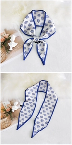 Detail view of a slim floral silk scarf with pointed ends and a refined blue border finish