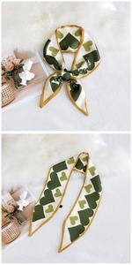 Detail of a green heart pattern silk scarf tied in a bow on a white textured background