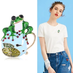 Spilla a forma di rana in smalto verde creativo con strass rossi su t-shirt bianca