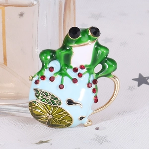 Dettaglio macro di una spilla rana in smalto verde con strass rossi e base a ninfea