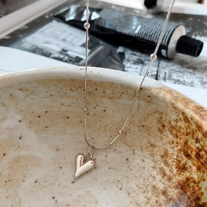 Close-up of minimalist silver heart pendant necklace hanging on a textured ceramic bowl