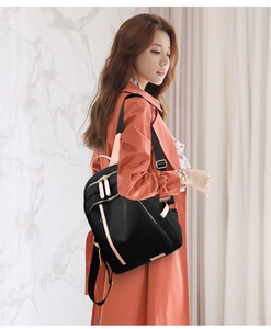 Vista lateral de mochila de nailon negro con correas rosas en modelo para viajes