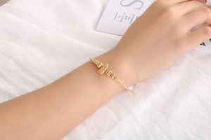 Detail eines goldenen Edelstahl-Perlenarmbands mit religiösem Anhänger und einer weißen Perle
