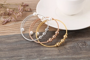 Three-color woven steel wire bracelets set with pearls and rhinestones on wooden table