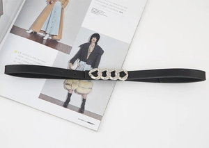 Détail d'une ceinture fine en cuir noir avec boucle à trois chaînes argentées sur un magazine