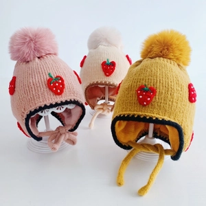 Detail of knitted baby hats with strawberry embroidery and plush pom-poms in three colors