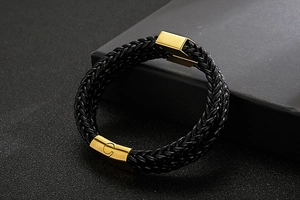 Macro detail of black braided leather bracelet with golden arrow magnetic clasp and G engraving