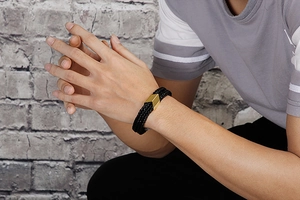 Close-up of black braided leather bracelet with golden magnetic clasp worn on a wrist