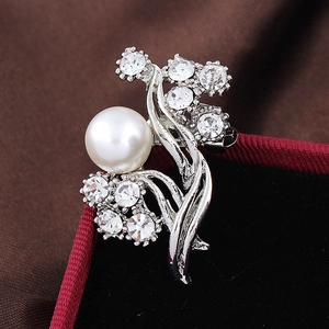 Macro shot of silver floral brooch with large white pearl and clear crystals on red velvet
