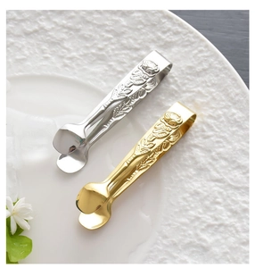 Close-up of 304 stainless steel sugar tongs with embossed rose pattern on a plate