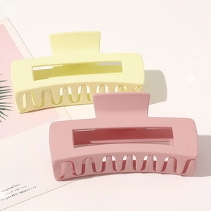 Close-up of large matte hair claws in yellow and pink with rectangular cutout design