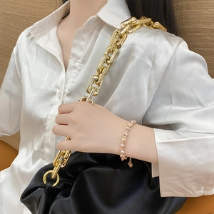 Close-up of 14K gold plated baroque pearl bracelet with elegant black cloud pleated handbag