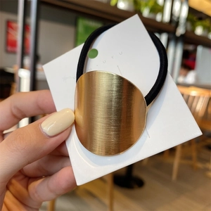 Detail of a minimalist gold brushed metal oval ornament on a black elastic hair tie