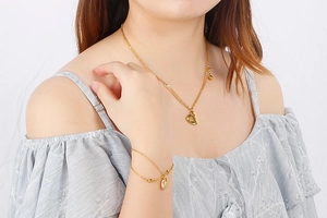 Detailed view of layered 18K gold-plated heart necklace and bracelet set on model