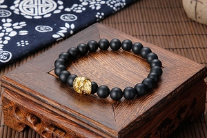 Close-up of matte black beads and gold skull charm on a vintage wooden pedestal