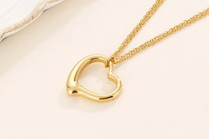 Detail of a gold double-layer chain necklace featuring a hollow heart pendant on fabric