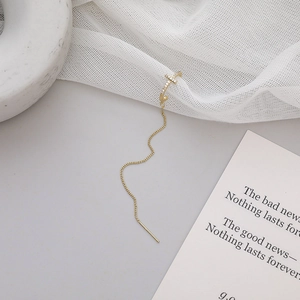 Dettaglio ear cuff a croce dorata con catena lunga e zirconi su sfondo grigio