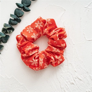 Detail of red velvet scrunchie with white snowflake patterns on a textured background