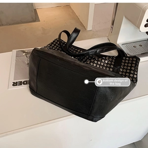 Detail view of the flat rectangular base with silver rivets on black tote bag